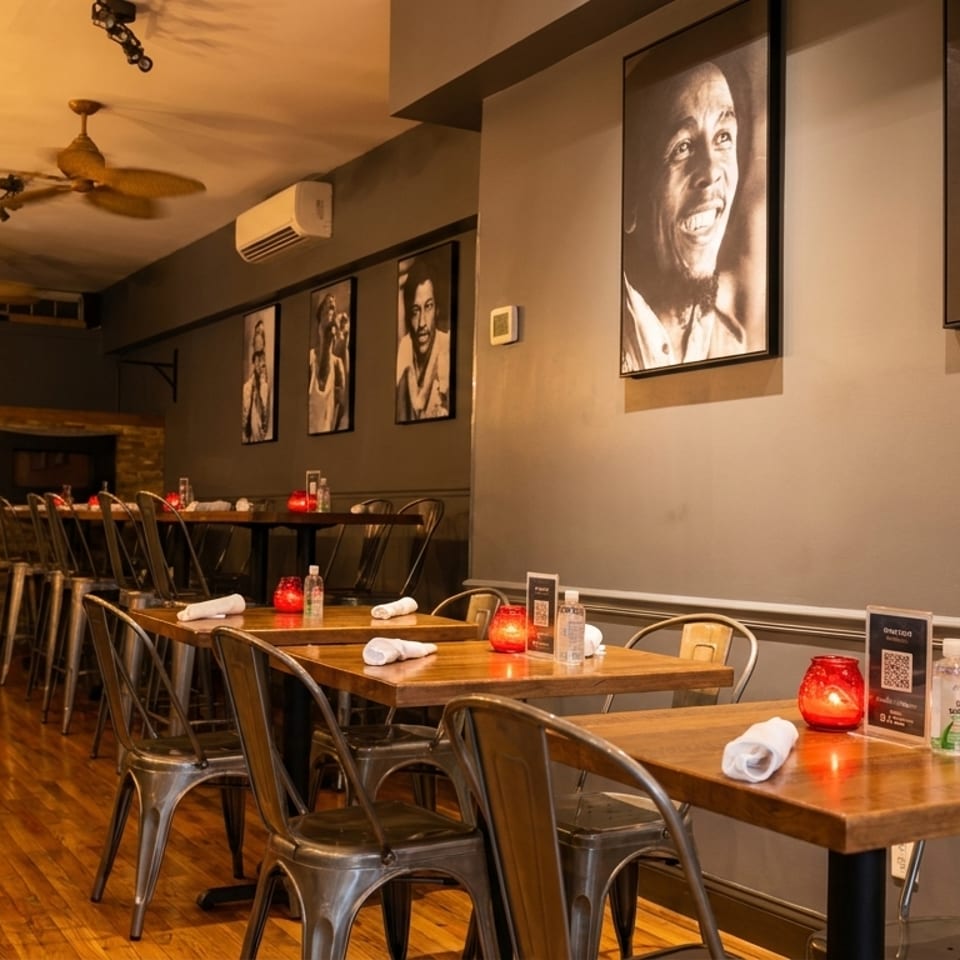 Restaurant interior with wooden tables, metal chairs, and framed black and white portraits on gray walls.