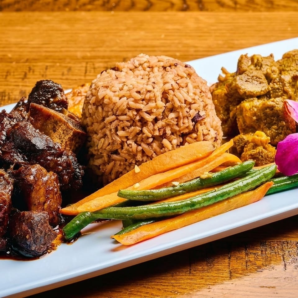 A white rectangular plate holds oxtail, curry goat, rice and peas, and steamed vegetables, garnished with an orchid.
