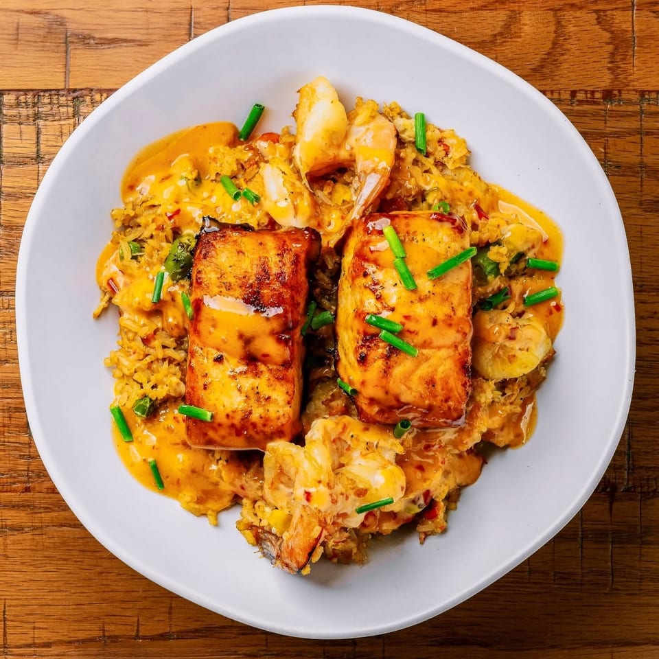 Two pieces of grilled salmon over rice and shrimp, drizzled with sauce and chives.