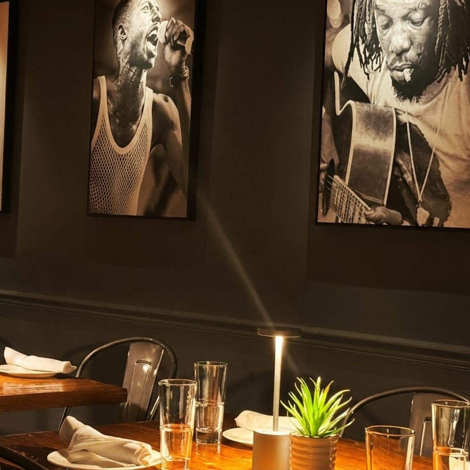 Restaurant dining room with dark walls, black and white art, and wooden tables with place settings.