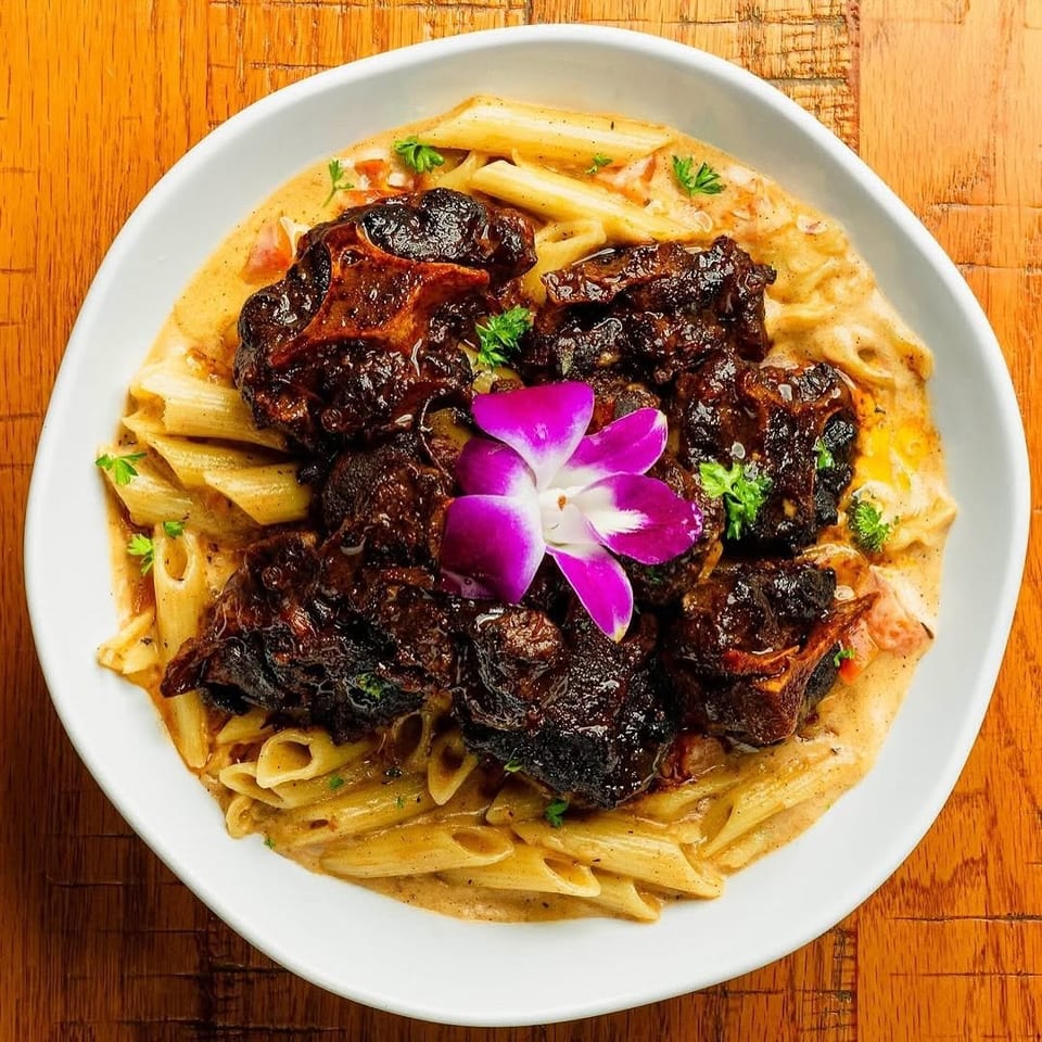 Oxtail pasta with penne, creamy sauce, garnished with parsley and a purple orchid.